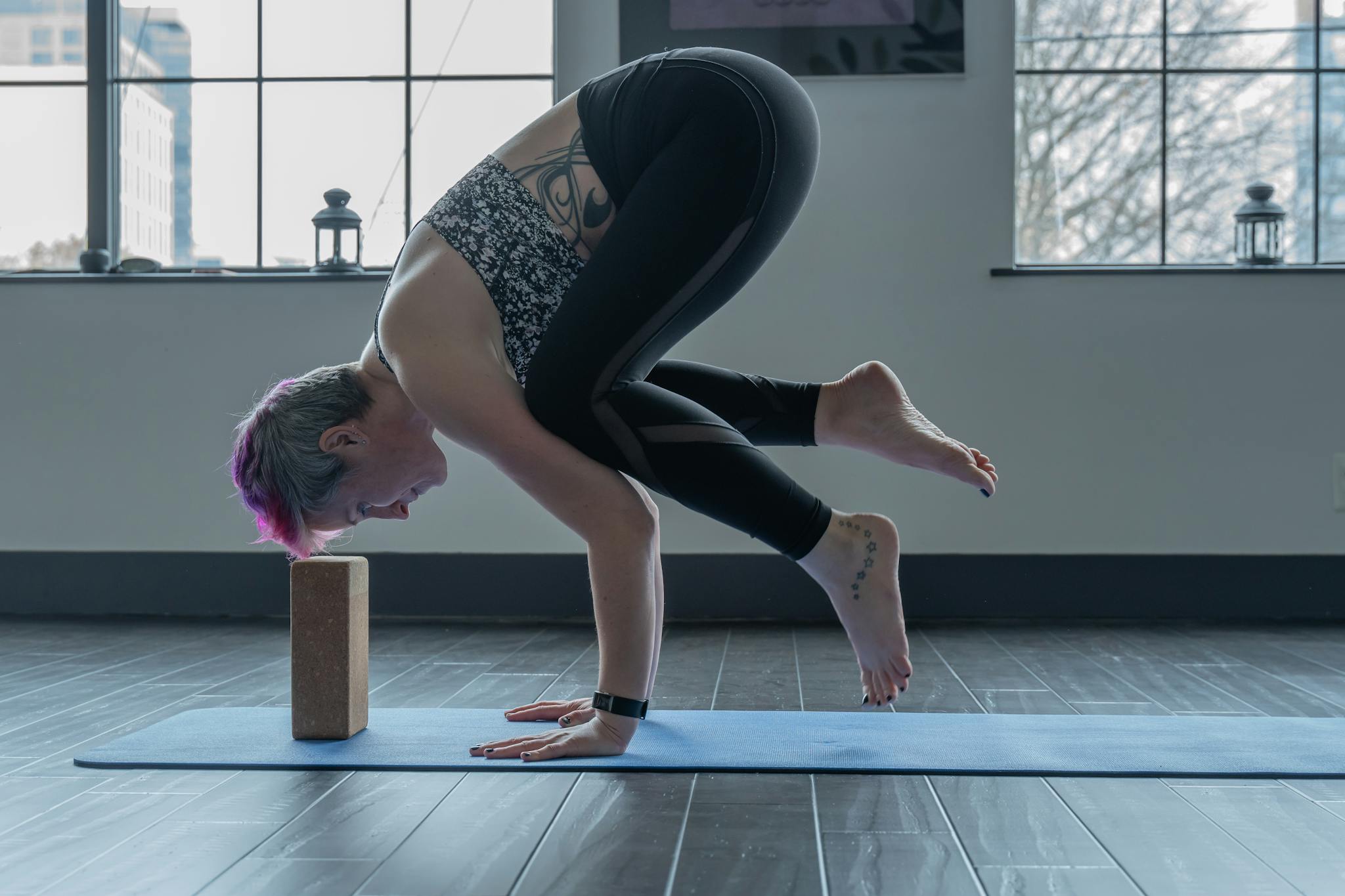 Woman performs advanced yoga pose indoors using a brick for balance, showcasing strength and flexibility.